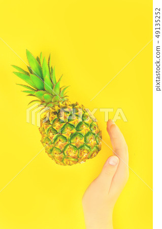 Hand with pineapple on summer yellow background Hand with pineapple on summer yellow background 49135252