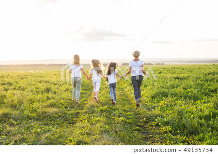 Family, summer and holiday concept - Group of women and girls going away in green field 49135734