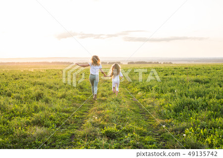 Family, summer and holiday concept - Back view of mother holding her daughter's hand running towards Family, summer and holiday concept - Back view of mother holding her daughter's hand running towards 49135742