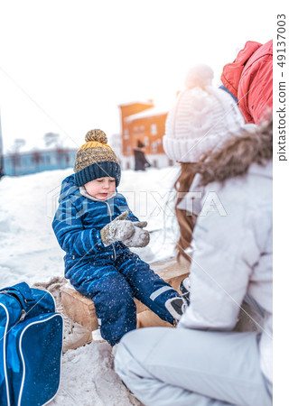 A small boy of 4-6 years old, sitting on a bench, in the winter in the city on the rink. Waiting for A small boy of 4-6 years old, sitting on a bench, in the winter in the city on the rink. Waiting for 49137003