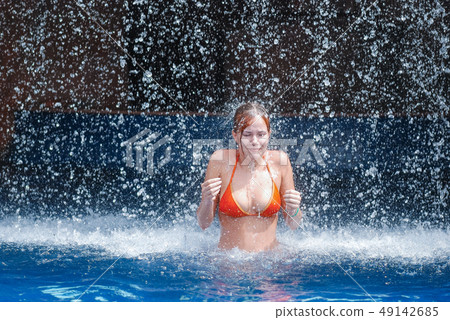 laughing and happy girl in an orange swimsuit plays jumping and having fun under a waterfall in the 49142685