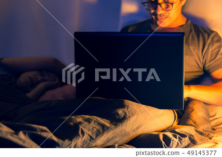 Man lying in bed and working with laptop late at night. Man lying in bed and working with laptop late at night. 49145377