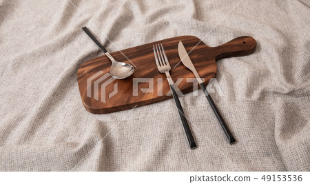 A knife, spoon, and fork on a cutting board 49153536