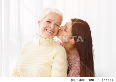 Young daughter kissing senior mother in cheek Young daughter kissing senior mother in cheek 49153554