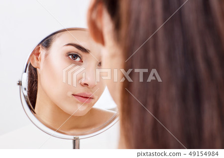 Woman with eyes bruises looks on her reflection in the mirror. 49154984