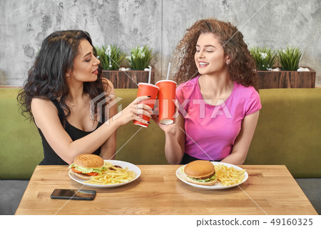 Pretty girls sitting in cafe and clinking paper cups. Pretty girls sitting in cafe and clinking paper cups. 49160325