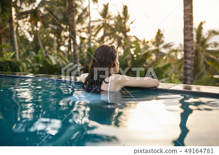 Woman in white swimsuit in outdoor pool on green jungle background Woman in white swimsuit in outdoor pool on green jungle background 49164781