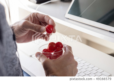 young man eating cherry tomatoes at the office 49166579