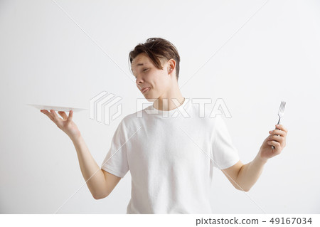 Young sad attractive guy holding empty dish and fork isolated on grey background. 49167034