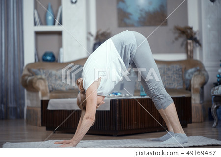 Adult Woman Over 50 Years Old Doing Yoga at Home in the Living Room. Adult Woman Over 50 Years Old Doing Yoga at Home in the Living Room. 49169437
