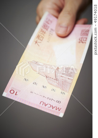 Macao currency Male hand with Pataca banknote 49174018