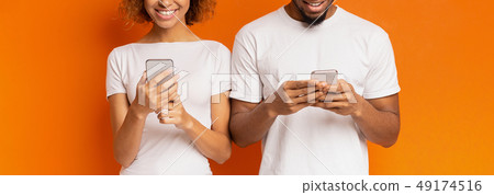 Cheerful black millennial couple browsing on cellphones Cheerful black millennial couple browsing on cellphones 49174516