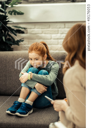 Cheerless unhappy girl putting chin on her knees 49176053