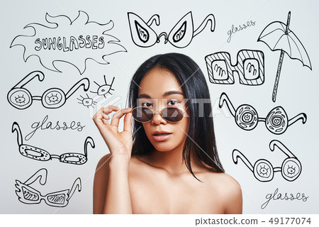 Fashion look. Portrait of attractive asian woman adjusting her sunglasses and looking at camera 49177074