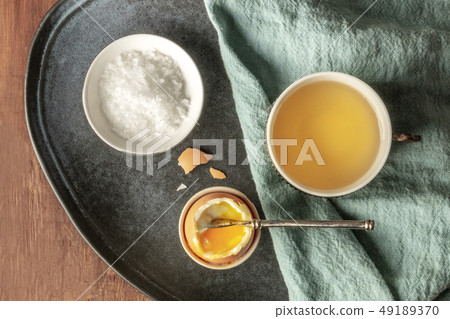 A soft-boiled egg with coarse sea salt and tea, shot from above on a dark rustic wooden background 49189370