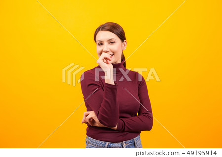 Charming caucasian woman smiling and bitting her thumb over yellow background 49195914