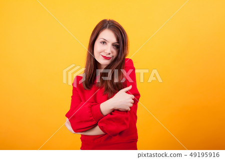 Portrait of cute young woman gives herself a hug over yellow background 49195916