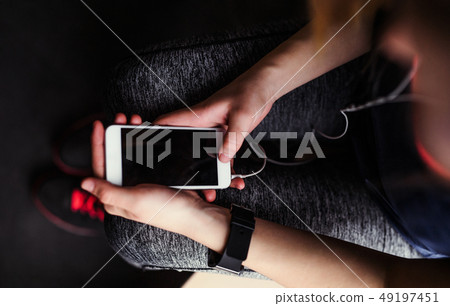 A midsection of young girl or woman with earphones and smartphone in a gym. A midsection of young girl or woman with earphones and smartphone in a gym. 49197451