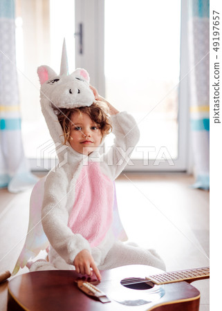 A portrait of small girl in unicorn mask with guitar at home. A portrait of small girl in unicorn mask with guitar at home. 49197657