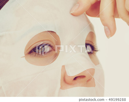 Woman applying sheet mask on face Woman applying sheet mask on face 49199288