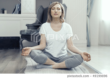 A Woman Over the Age of 50 is Doing Yoga at Home. 49199896