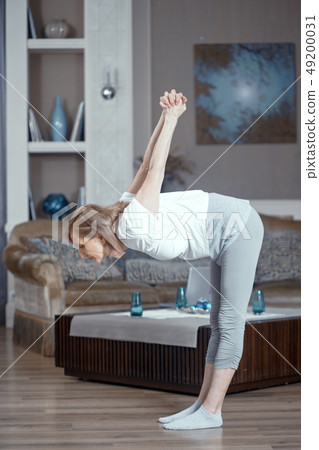 A 50 Year Old Woman Practices Yoga at Home in the Living Room. A 50 Year Old Woman Practices Yoga at Home in the Living Room. 49200031