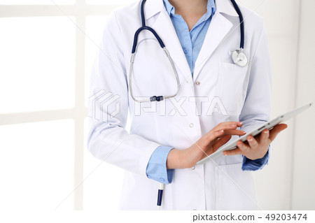 Woman doctor using tablet computer while standing straight in hospital closeup. Healthcare 49203474