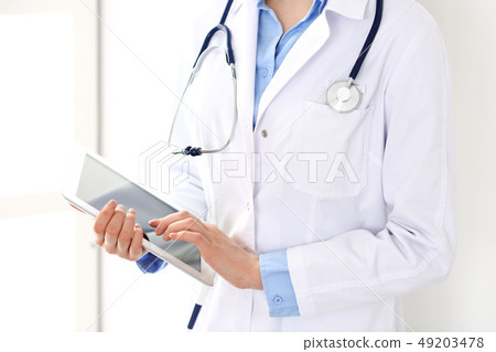 Woman doctor using tablet computer while standing straight in hospital closeup. Healthcare Woman doctor using tablet computer while standing straight in hospital closeup. Healthcare 49203478