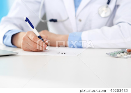 Female doctor filling up prescription form while sitting at the desk in hospital closeup. Healthcare 49203483