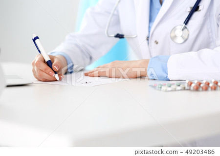 Female doctor filling up prescription form while sitting at the desk in hospital closeup. Healthcare 49203486