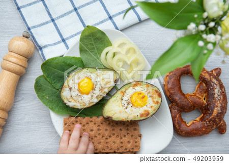 Eggs baked in avocado on plate with with a stretching child's hand 49203959