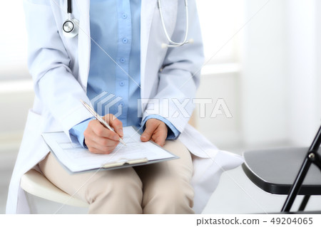 Female doctor writing up medication history records form on clipboard, while sitting at the chair 49204065