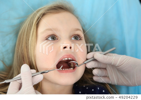 Little baby girl sitting at dental chair with open mouth and feeling fear during oral check up while Little baby girl sitting at dental chair with open mouth and feeling fear during oral check up while 49204229