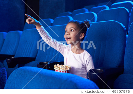 African girl poiniting with finger at screen in cinema. African girl poiniting with finger at screen in cinema. 49207976