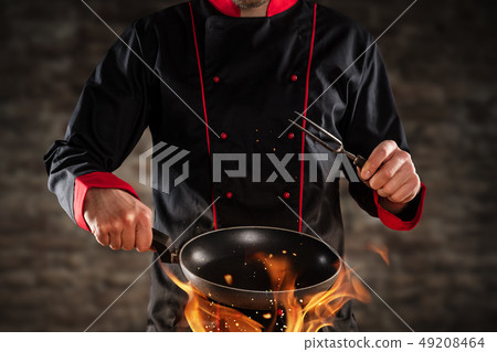 Closeup of chef holding frying pan above grill. 49208464