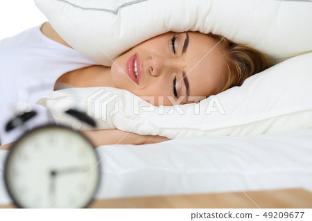 Young beautiful blonde woman lying in bed suffering from alarm clock sound Young beautiful blonde woman lying in bed suffering from alarm clock sound 49209677