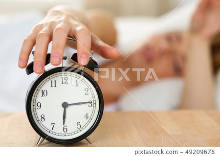 Stretching hand of sleepy young woman trying kill alarm clock Stretching hand of sleepy young woman trying kill alarm clock 49209678