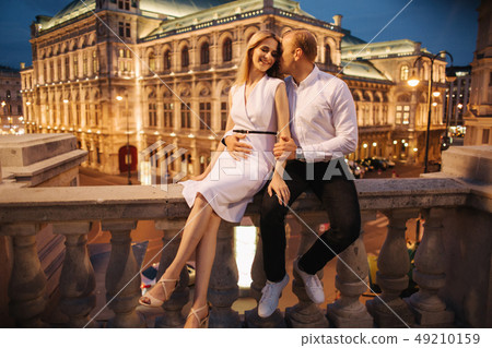 Wife and husband sist on the border in front of bilding with lights. Evening in the city. Night Wife and husband sist on the border in front of bilding with lights. Evening in the city. Night 49210159