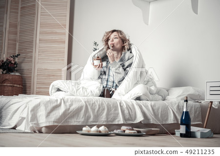 Young stressed woman eating sweets and drinking alcohol in bed 49211235