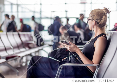Female traveler talking on cell phone while waiting to board a plane at departure gates at asian 49211802
