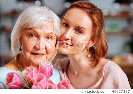 Portrait photo of mature daughter hugging grey-haired mother holding tulips 49227357