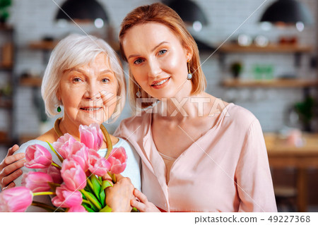 Appealing lady cuddling aged mom with bunch of tulips 49227368