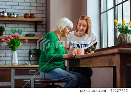 Alluring lady reading out Bible book for religious pensioner 49227725