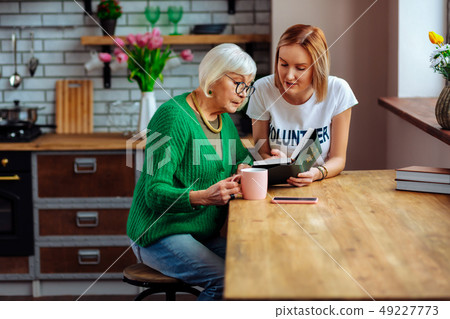 Pensioner listening to young lady reading Bible sitting at table 49227773