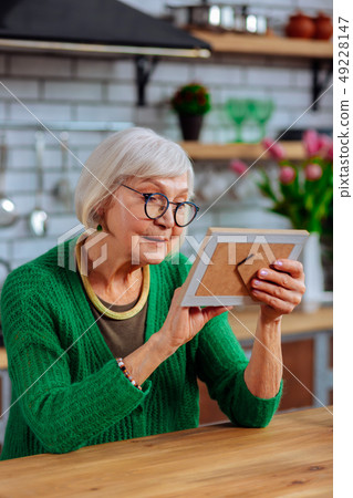 Aging lady lovingly looking at picture sitting at kitchen table 49228147