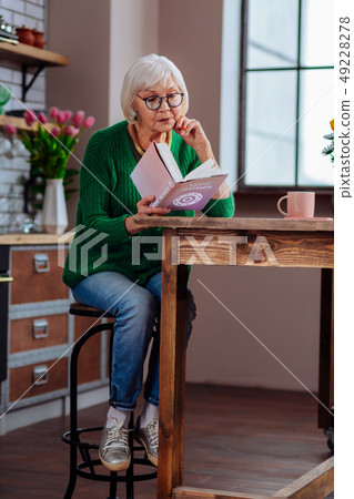 Aging woman being absorbed in book sitting at furnished kitchen 49228278