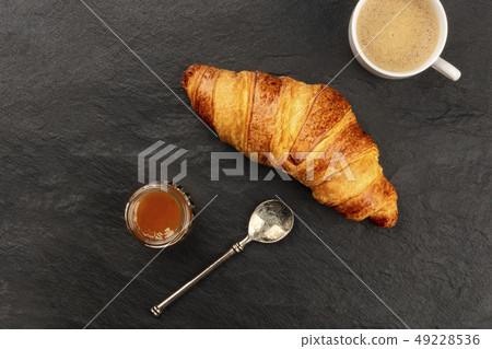 A closeup photo of a croissant with a cup of coffee and a jar of jam on a black background with a A closeup photo of a croissant with a cup of coffee and a jar of jam on a black background with a 49228536