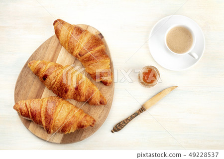 A high key photo of croissants with a cup of coffee and a jar of jam, shot from above on a white 49228537