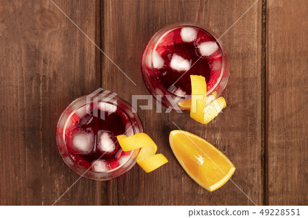 Two vibrant cocktails with campari and orange curl garnishes, with ice cubes and an orange slice 49228551