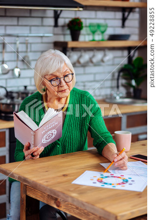 Focused white-haired madam studying vedic tables holding vedic book 49228855